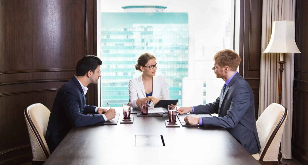 Portrait of young female business leader sitting in modern office and having meeting with her team. She showing something on tablet computer and asking questions