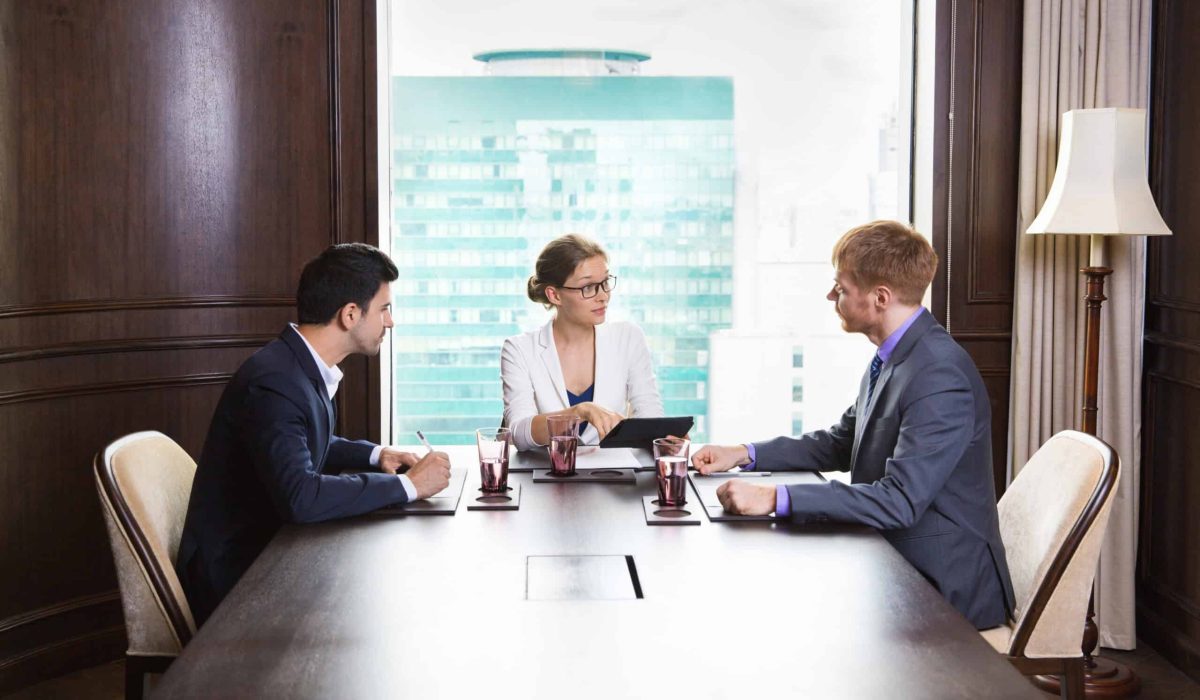Portrait of young female business leader sitting in modern office and having meeting with her team. She showing something on tablet computer and asking questions